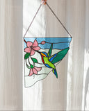 Person holding a stained glass panel with floral and bird design in front of a sheer curtain.