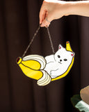 Hand holding a decorative item shaped like a cat on a banana with a blurred background