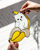 Hand holding a cartoon dog inside a banana with a blurred outdoor background