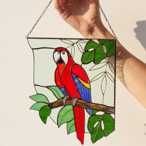 Hand holding a stained glass panel with a parrot design against a plain background