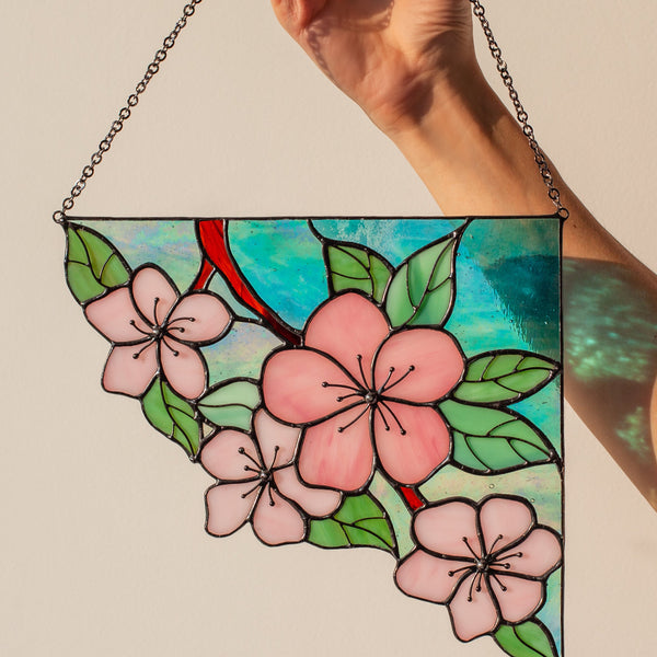 Hand holding a stained glass panel with floral design against a plain background