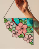 Hand holding a stained glass panel with floral design against a plain background