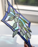 A stained glass suncatcher featuring an olive branch design with green leaves and iridescent pastel panels, held by a hand in front of a window.