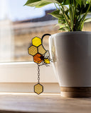 Decorative glass honeycomb and bee ornament on a white mug with a plant in the background.