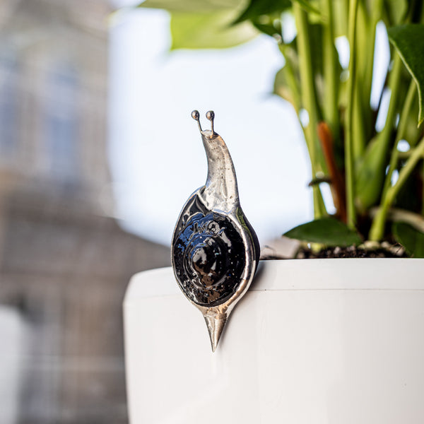 Decorative snail-shaped object on a white surface with a blurred plant and building in the background