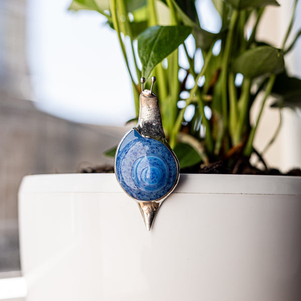 White ceramic pot with a small plant and decorative snail on a wooden surface
