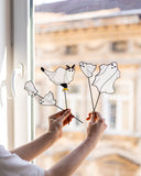 Person holding up decorative window stickers of cats and birds in front of a window.