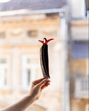 Person holding a small figurine of a woman with outstretched arms in front of a window with a blurred cityscape.