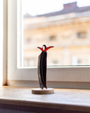 Decorative sculpture of a bird on a stand in front of a window with a blurred building view.