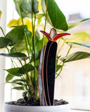 Small decorative sculpture of a bird perched on a branch placed among potted plants.