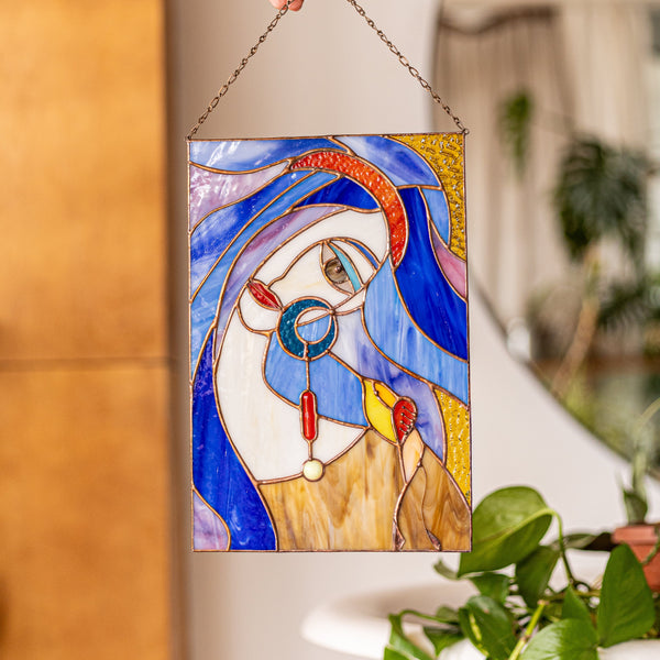 Stained glass panel of a face held by a hand with a blurred indoor background