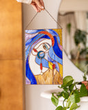 Stained glass panel of a face held by a hand with a blurred indoor background
