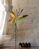 Decorative stained glass bird of paradise flower on a stand against a neutral background