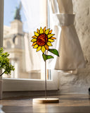Decorative sunflower sculpture on a stand in front of a window with light curtains.