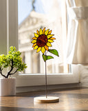 Sunflower-shaped decorative item on a wooden base in a room with a window and plant.