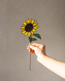 Hand holding a stained glass sunflower against a plain background