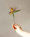 Hand holding a stained glass flower against a plain background
