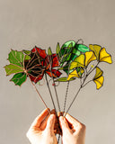 Stained glass leaf sculpture held by hands against a neutral background