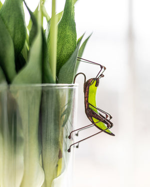 Decorative glass vase with green leaves and a small metal sculpture on a white background