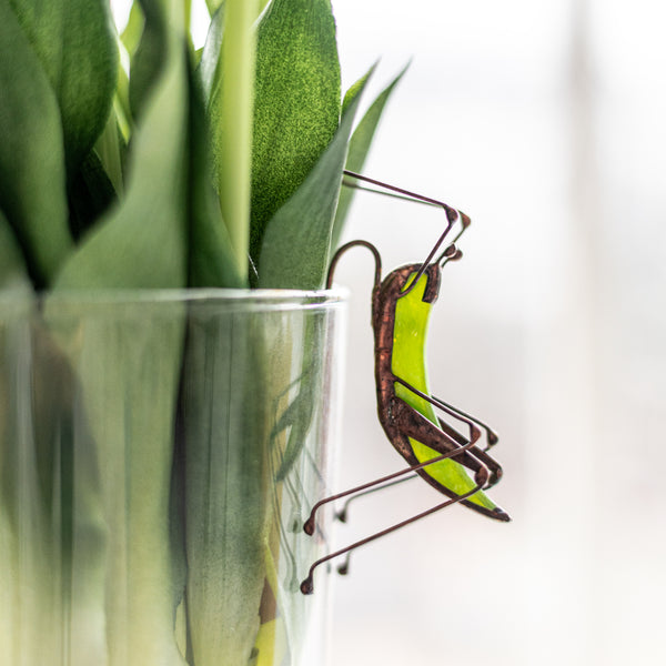 Decorative glass vase with green leaves and a small metal sculpture on a white background