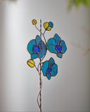 Stained glass flower decoration with blue flowers and yellow leaves on a blurred background