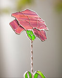 Stained glass flower with pink petals and green leaves on a blurred background