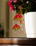Decorative mushroom ornament with red and gold polka dot design in front of a white pot with pink flowers.