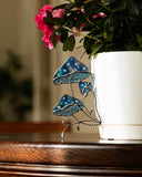 Decorative glass leaf sculpture in front of a potted plant with pink flowers.