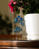 Decorative glass piece with blue and green design next to a white pot with pink flowers.