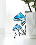 Stained glass blue mushroom decoration on a white surface with a plant in the background