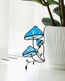 Stained glass blue mushroom decoration in front of a white planter with green plant