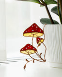 Decorative stained glass mushrooms on a white surface with a plant in the background