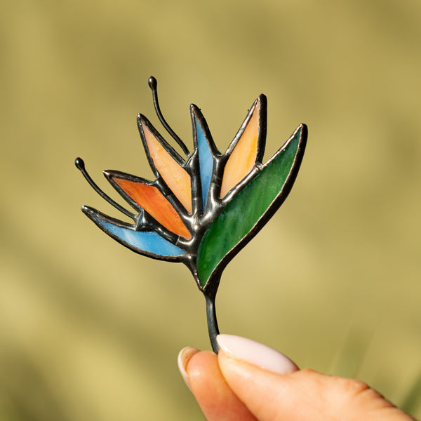 Hand holding a colorful glass leaf against a blurred natural background