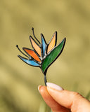 Hand holding a colorful glass leaf against a blurred natural background