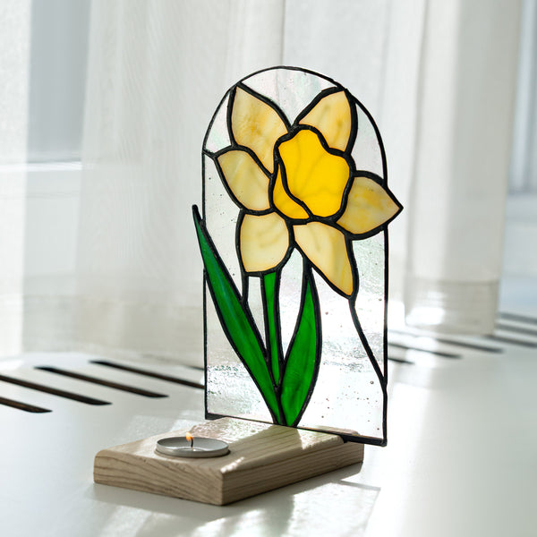 Stained glass daffodil lamp on a wooden base with white curtains in the background