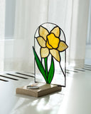 Stained glass daffodil lamp on a wooden base with white curtains in the background