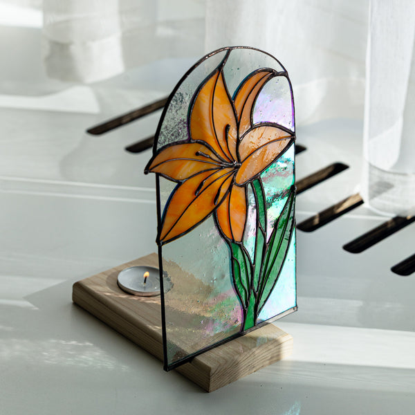 Stained glass flower design on a wooden base with a candle inside, placed on a reflective surface.