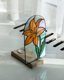 Stained glass flower design on a wooden base with a candle inside, placed on a reflective surface.