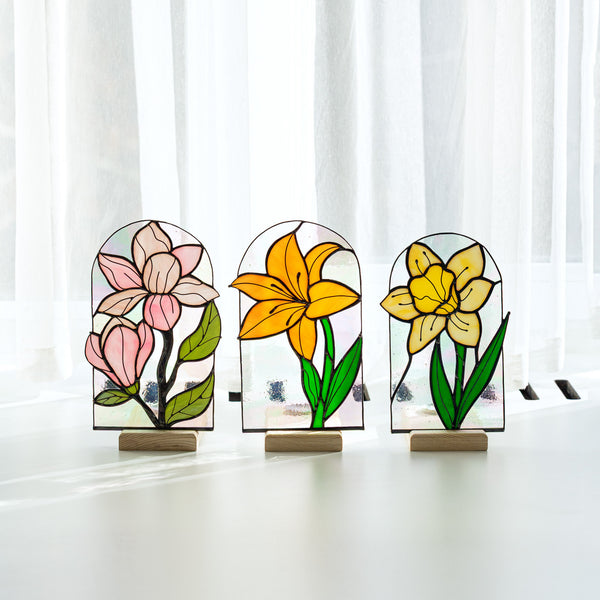 Three stained glass flower sculptures on a white surface with a white curtain background