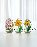 Three stained glass flower sculptures on a white surface with a white curtain background