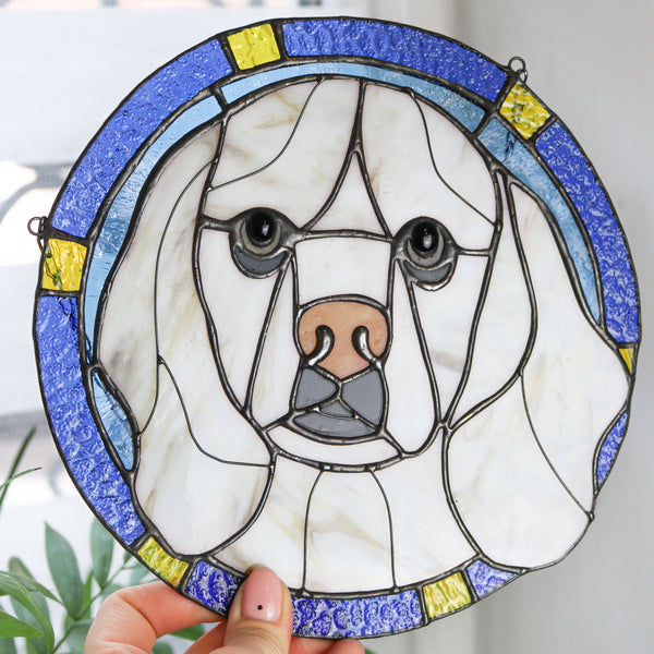 Stained glass window panel of a dog held by a hand with a blurred background