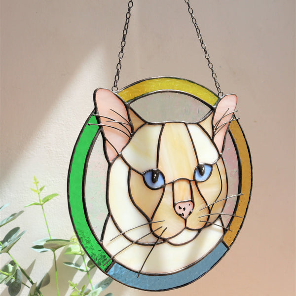Stained glass panel of a cat held by a hand against a neutral background