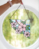Stained glass panel with floral design held by a hand against a blurred green background