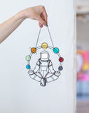 Person holding a wall decal of a meditating figure with chakra colors against a white wall.