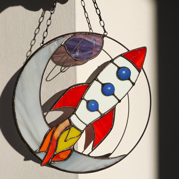 Stained glass panel with a rocket design held by a hand.