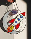 Stained glass panel with a rocket design held by a hand.