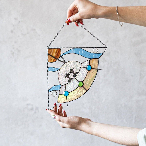 Person holding a stained glass panel with a colorful design against a plain background