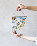 Person holding a stained glass panel with a colorful design against a plain background