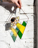 Hand holding a colorful geometric stained glass panel against a white brick wall.