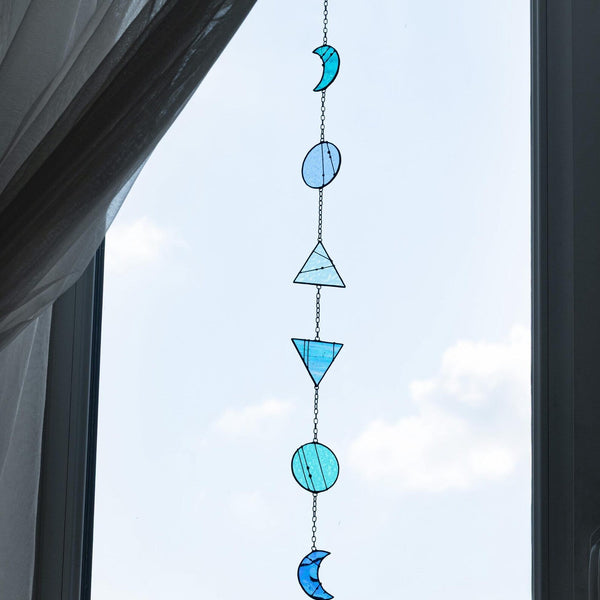 Decorative glass hanging with blue and green shapes in front of a window